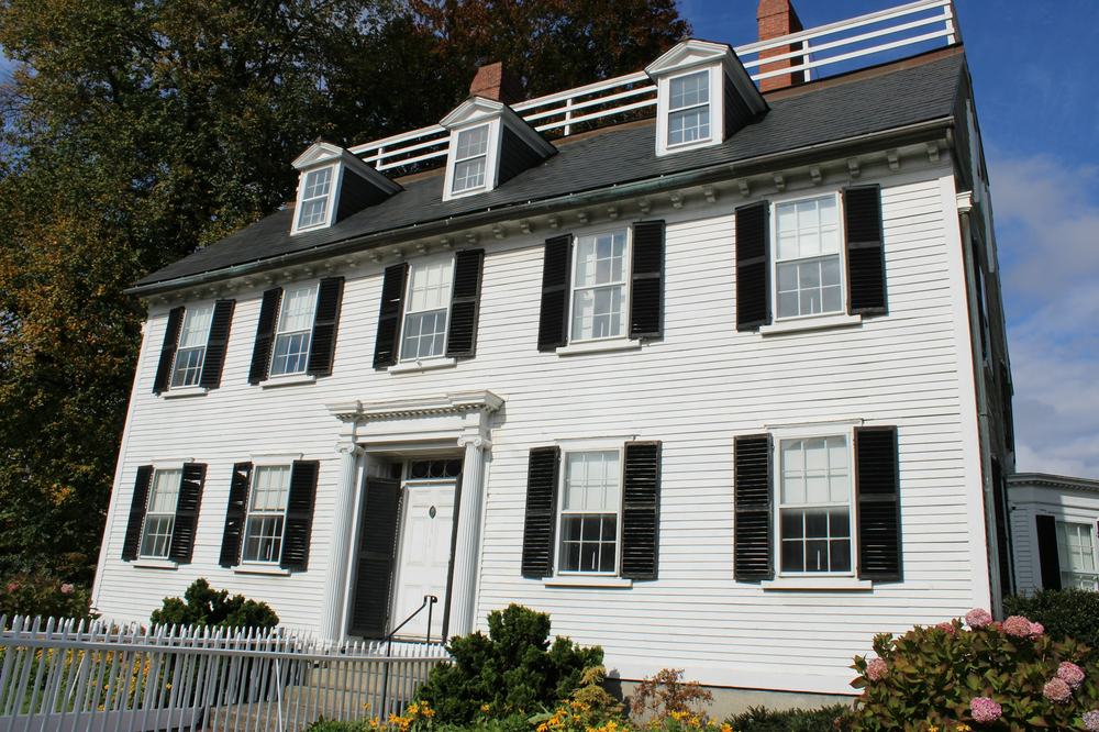 A white clapboard colonial house with black shutters and dormers